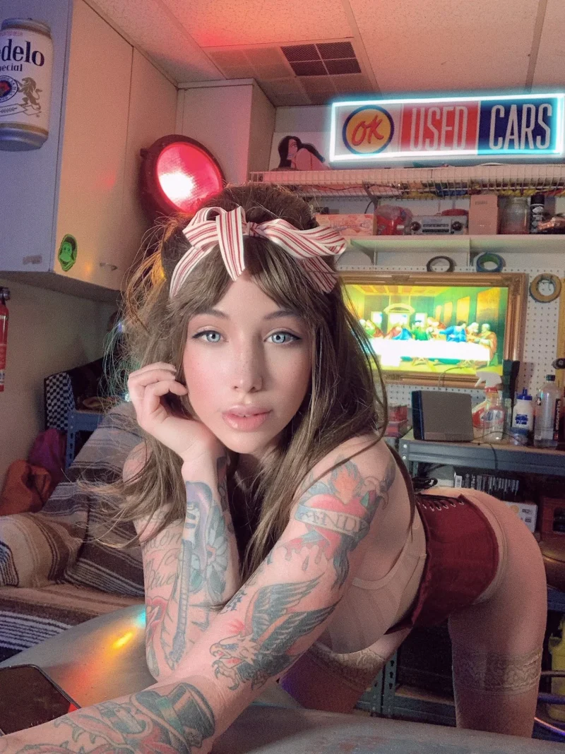 Tattooed Coconut Kitty in red shorts leans on counter with bow in hair