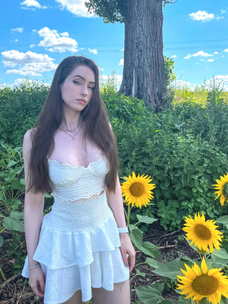 Seductive Anastasiia Mut in white eyelet dress posing by sunflowers under blue sky